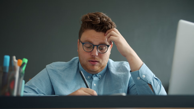 Man with glasses looking stressed at desk